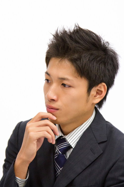 水色の壁の前で腕を組んで横目で様子をうかがうサラリーマン