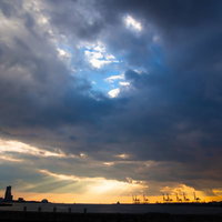 厚い雲の隙間から漏れるオレンジの夕焼けの光の写真