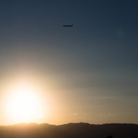 夕焼けのオレンジの空を横切る飛行機のシルエットの写真