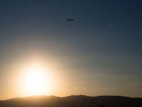 夕焼けのオレンジの空を横切る飛行機のシルエット