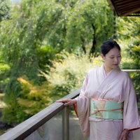 日本庭園の縁側に手を置く着物の女将さんの写真