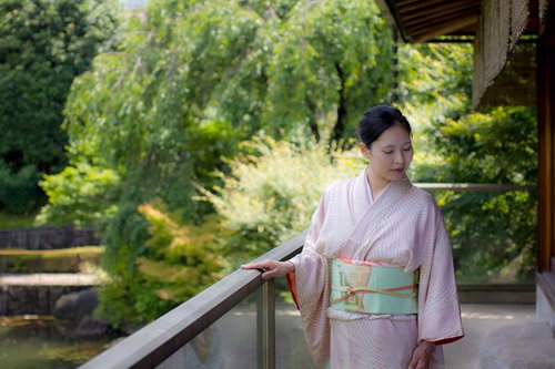 日本庭園の縁側に手を置く着物の女将さん