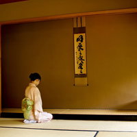 掛け軸のある和室で正座する着物の女性の写真