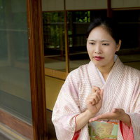 縁側で手を組んで悩む着物の女将さんの写真