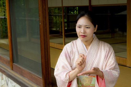 縁側で手を組んで悩む着物の女将さん