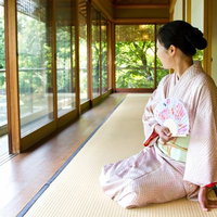 緑が見える廊下で扇子を持ち座る着物の女性の写真