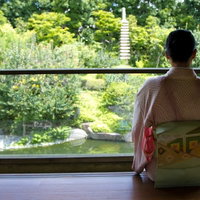 縁側から日本庭園の池を眺める着物の女性の写真