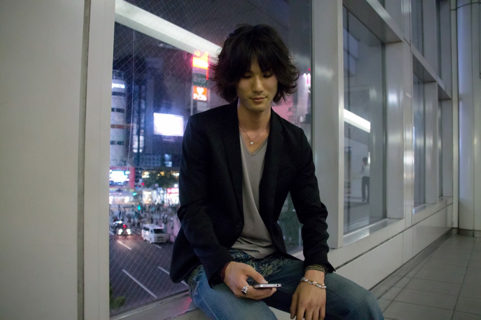 夜の通路で座ってスマホをいじる若者［モデル：村田裕章］