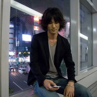 夜の通路で座ってスマホをいじる若者の写真