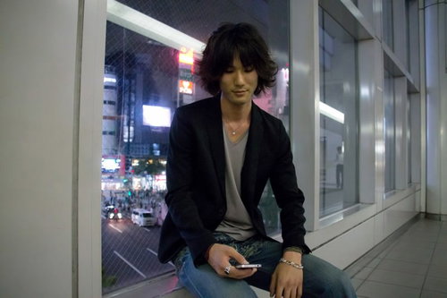 夜の通路で座ってスマホをいじる若者