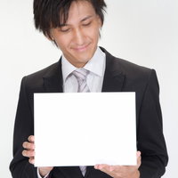 白いボードを手に持って内容を確認するスーツ姿のビジネスマンの写真