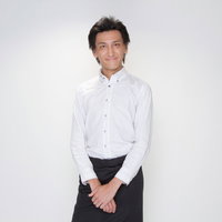 白いシャツに黒いエプロンの笑顔で立つウェイターの男性の写真