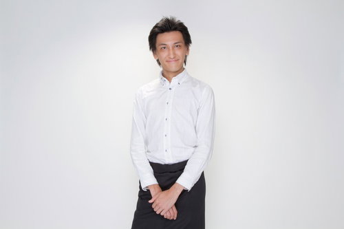 白いシャツに黒いエプロンの笑顔で立つウェイターの男性