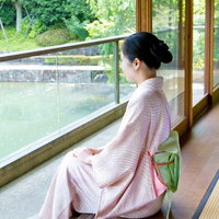 庭の緑を背景に縁側に座る着物姿の女性の横顔の写真