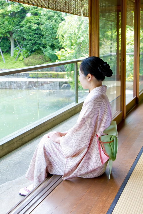 庭の緑を背景に縁側に座る着物姿の女性の横顔