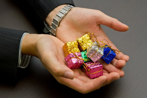 「ほら、ご褒美だよ」とプレゼントの箱を差し出すスーツ姿の手元