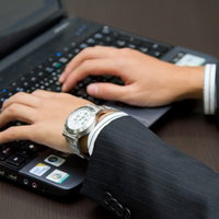 木目の机でノートPCのキーボードを操作するスーツのビジネスマンの写真