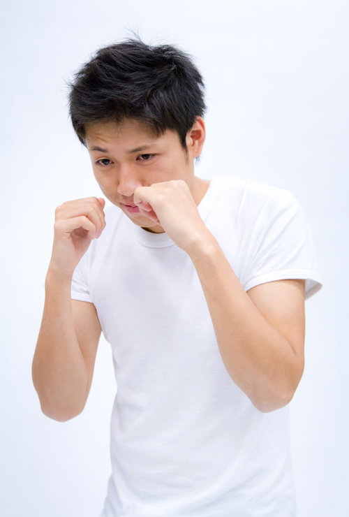 白い背景の前で構えてシャドーボクシングする男性