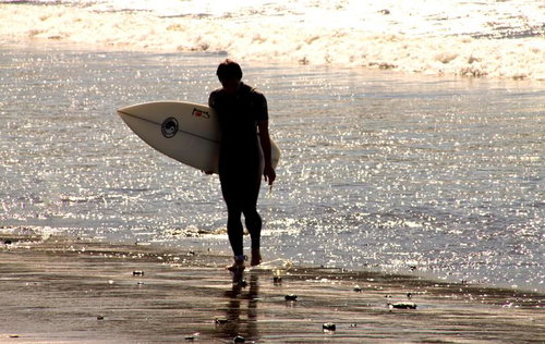 サーフボードを抱えて波打ち際の砂浜を歩くサーファー