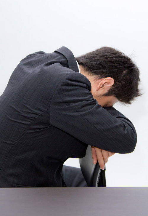 椅子の背もたれに体を預けてうなだれるスーツのビジネスマン