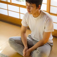畳の座敷であぐらをかいてくつろぐ甚平姿の週末の男性の写真