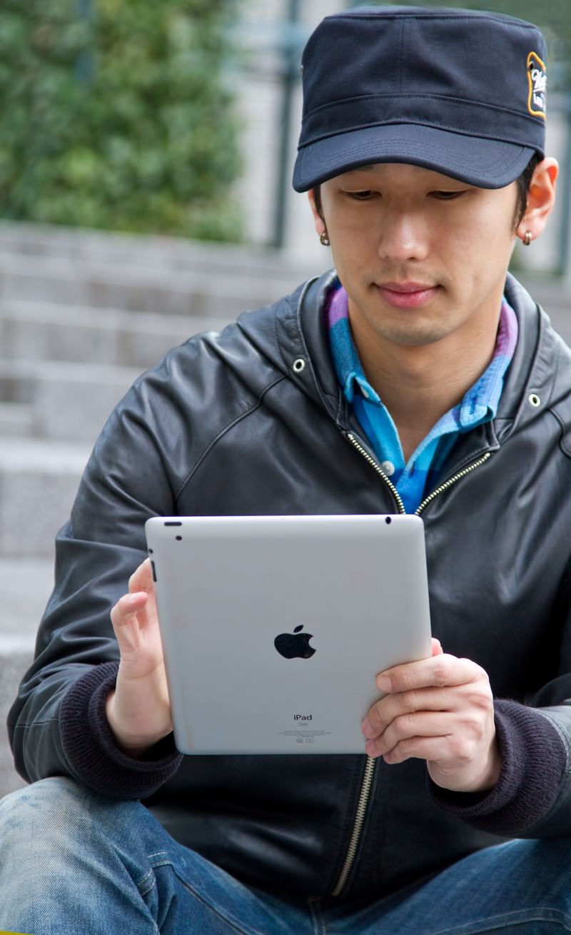 屋外の階段でiPadを両手で持つ男性［モデル：大川竜弥］