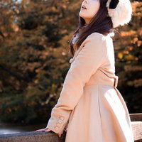 赤や黄色に色づいた紅葉の木々を見上げるコートの女性の写真