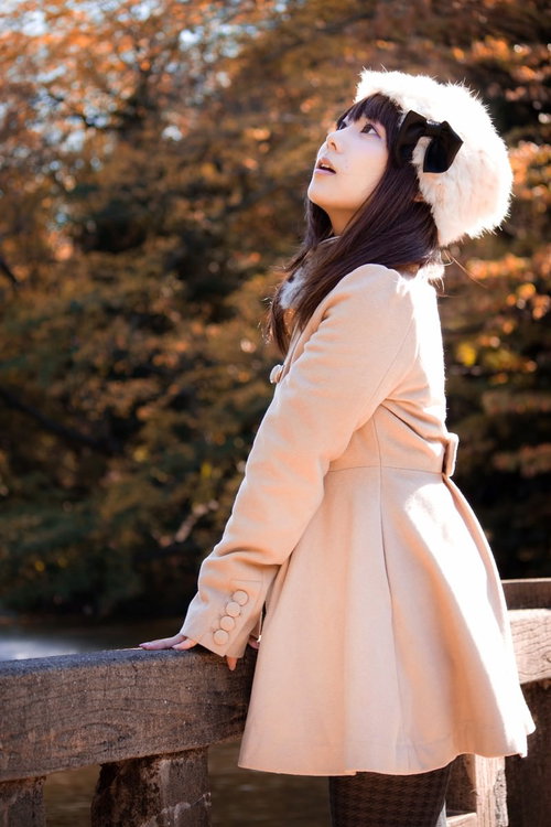 赤や黄色に色づいた紅葉の木々を見上げるコートの女性