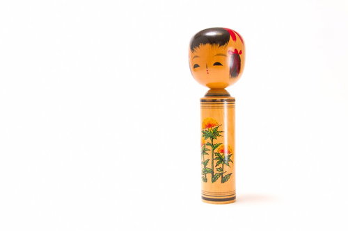 丸い頭と赤い模様が描かれた木製のこけしの置物