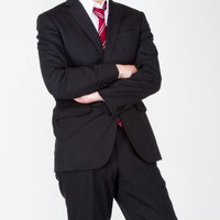 水色の壁の前で真剣な表情で腕を組むスーツ姿の男性の写真