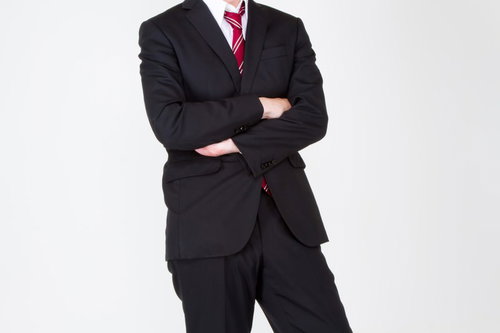 水色の壁の前で真剣な表情で腕を組むスーツ姿の男性