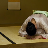 和室で深々と頭を下げ礼をする着物の女将の写真