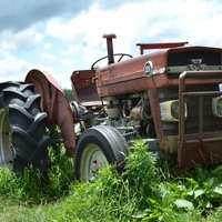田園風景の中に置かれた古い赤茶色の耕運機の写真