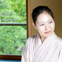 窓辺に座り庭の緑を見る着物の女性の写真