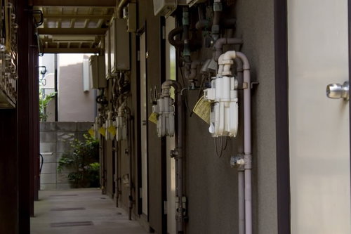 配管やメーターが並ぶ薄暗いアパートの廊下