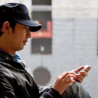 帽子をかぶって片手でスマホを操作するカジュアルな男性の写真