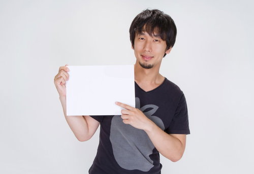 「ご案内」の白いボードを正面に持つ笑顔の男性