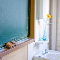 教室の緑の黒板の前に花瓶の花が飾られた教卓の写真