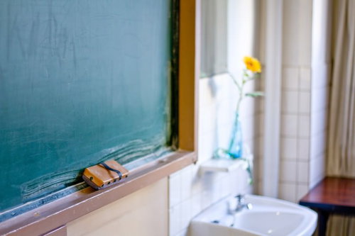 教室の緑の黒板の前に花瓶の花が飾られた教卓