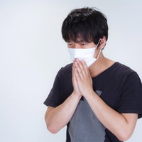 半袖のTシャツの上から不織布マスクをする男性の写真