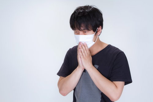 半袖のTシャツの上から不織布マスクをする男性