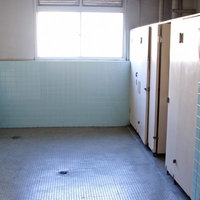 白いタイルの壁と個室が並ぶ学校のトイレの内部の写真