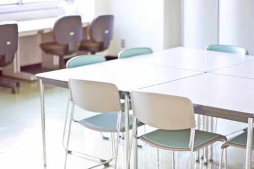 灰色のパイプ椅子と長机が並ぶ会議室や教室の風景