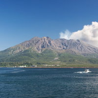 雲の中から白い噴煙をもくもくと上げる桜島の山頂の写真