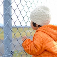 金網のフェンスの目に指をかけてしがみつく子供の手の写真