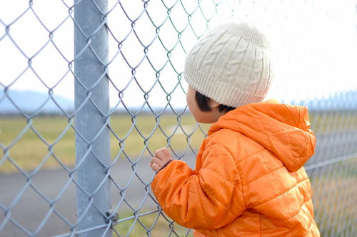 金網のフェンスの目に指をかけてしがみつく子供の手