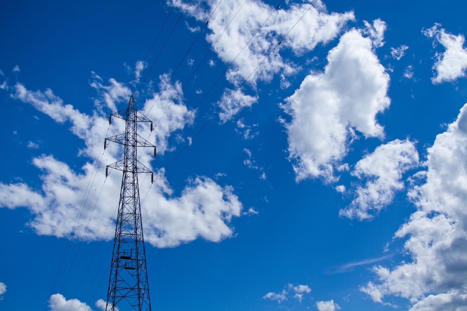 青空と白い雲の下にそびえる送電線の鉄塔