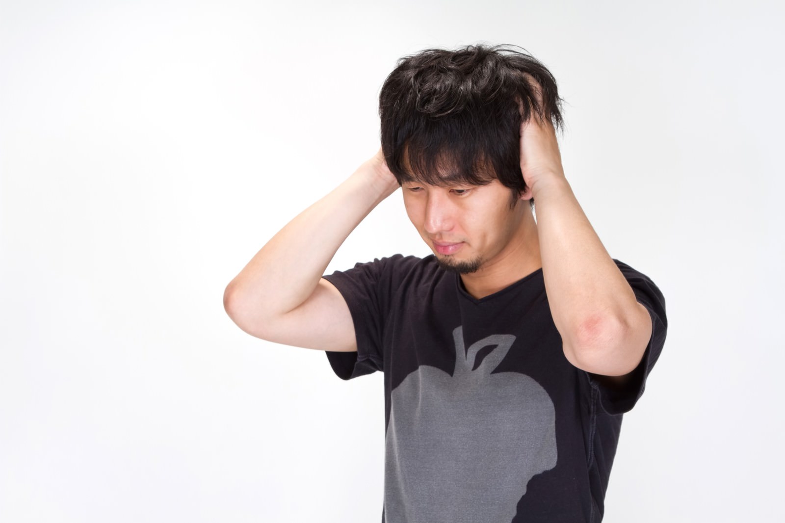 悩んで両手で頭をかきむしる黒Tシャツの男性［モデル：大川竜弥］