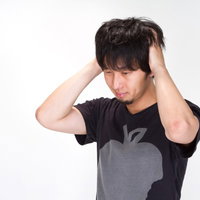 悩んで両手で頭をかきむしる黒Tシャツの男性の写真