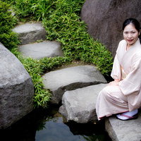 日本庭園の池の踏石にしゃがみこむ着物の女性の写真